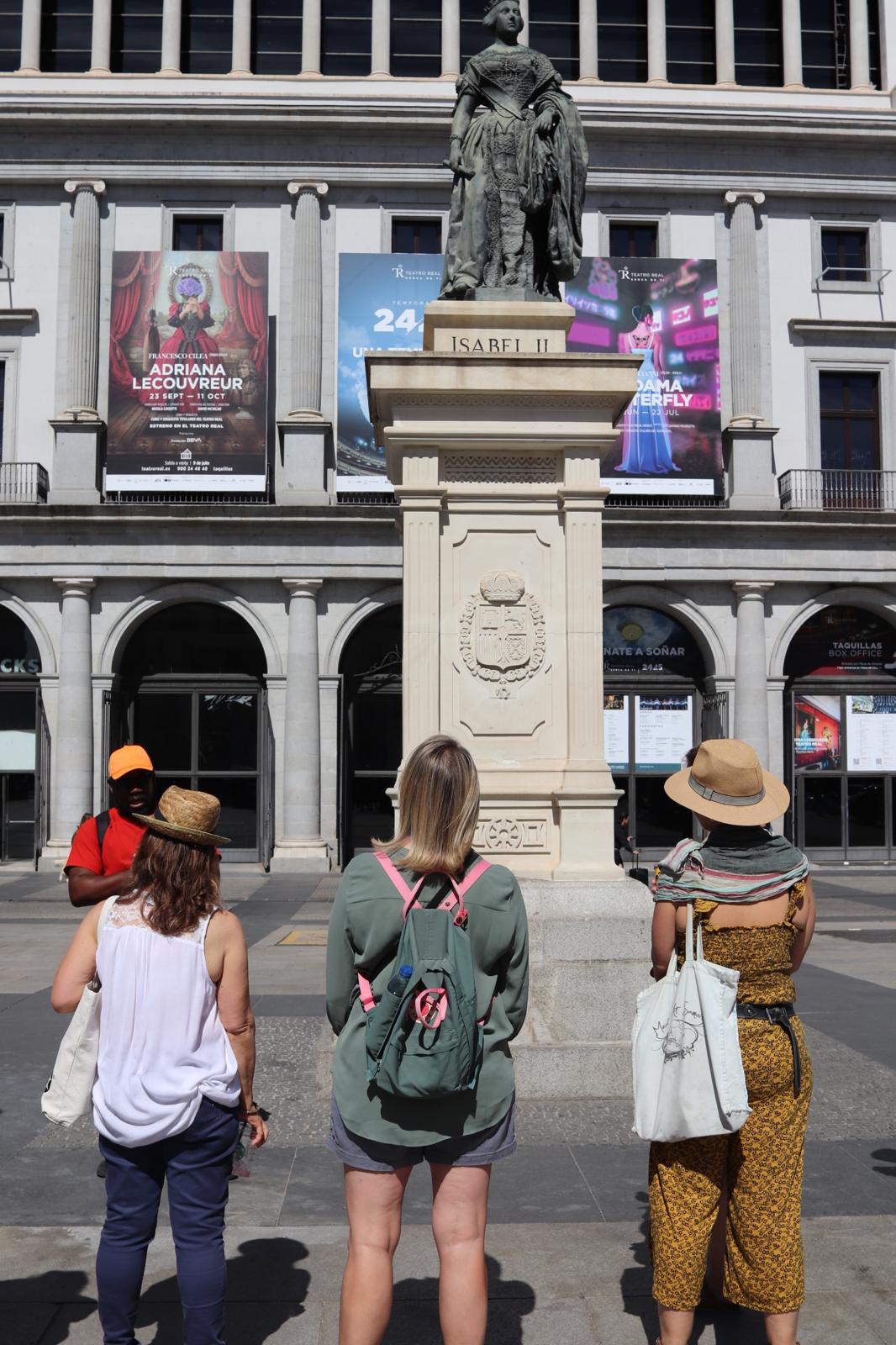 Imagen de tres mujeres observando y escuchando la explicación de nuestro guía frente a una estatua de Isabel II.
